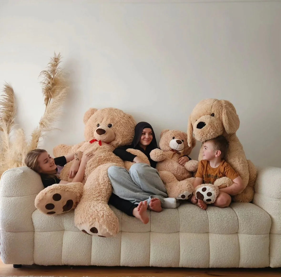 Three kids are hugging their giant teddy bear and dog plush toy on a couch.